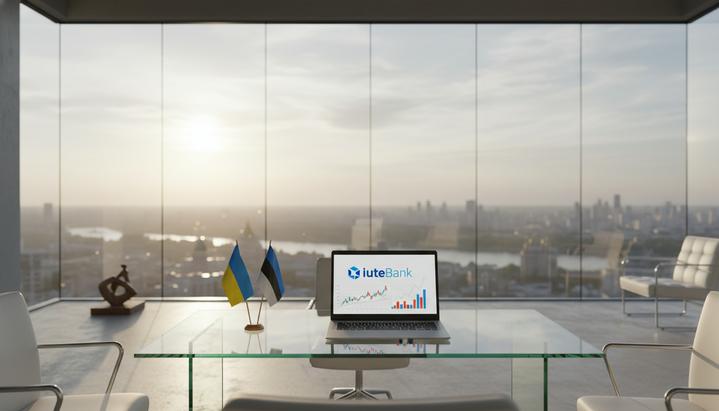 Современный пустой офис с панорамным видом на утренний Киев. На стеклянном столе стоит ноутбук с логотипом IuteBank и флагами Украины и Эстонии.