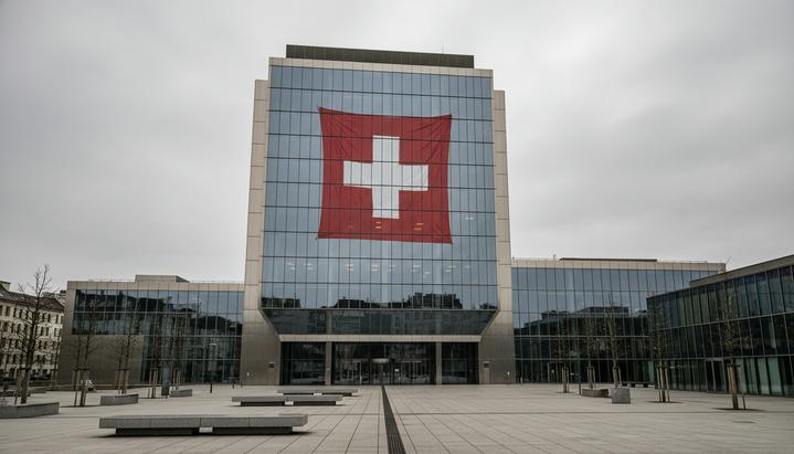 Современный стеклянный фасад штаб-квартиры крупного швейцарского банка в Цюрихе в пасмурный день, в котором отражается швейцарский флаг.